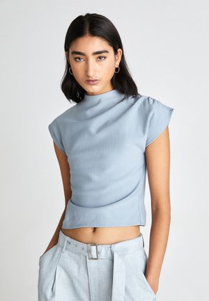 Light blue, cropped top with a high neckline and cap sleeves, made of smooth fabric; paired with light gray, tailored pants featuring a buckle.