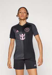 Black soccer jersey with pink accents, featuring a crew neck, short sleeves, and a logo. Worn with matching black shorts.
