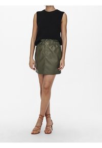 Black sleeveless knit top, green faux leather skirt with elastic waistband and button details, paired with brown strappy sandals.