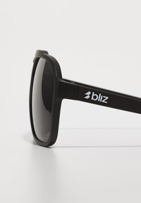 Black plastic sunglasses with a matte finish, square frame, and dark lenses. Features a white logo on the temple.