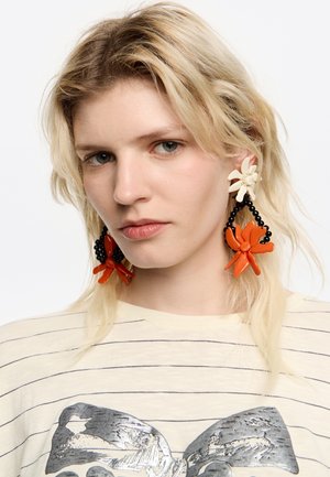 Colorful statement earrings featuring red and black floral shapes, with black beads as accents, and a textured finish.