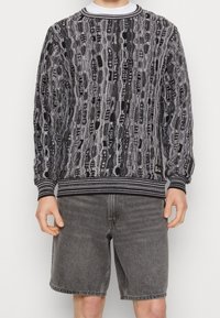 Schwarzer und grauer gemusterter Pullover mit strukturiertem Strickdesign, gerippten Bündchen und rundem Halsausschnitt, kombiniert mit grauen Jeansshorts.