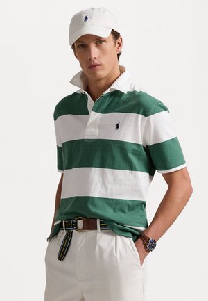 Grøn- og hvidstribet polo-shirt med krave, korte ærmer og et lille logo. Sammen med hvide bukser og et brunt bælte.