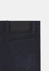 Mörka denimjeans med en texturerad, svart lädermidja som har en präglad "DIESEL"-logotyp. Inkluderar en distinkt spetsig baksidaficka-design.