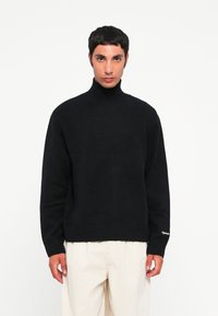 Suéter negro de cuello alto grueso con puños y dobladillo acanalados, fabricado en un material suave, que presenta una ligera textura y detalles de diseño mínimos.