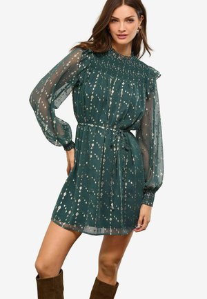 Rochie teal cu mâneci lungi transparente, accente volanate și detalii smockate. Prezintă un talie legată și modele florale metalice. Lungime scurtă.