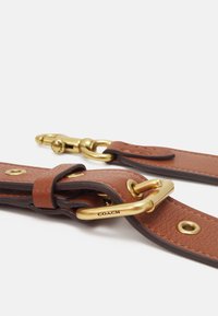 Cintura in pelle marrone con hardware in tono oro, caratterizzata da una finitura testurizzata, chiusura a fibbia e accenti circolari. Contrassegnata "COACH."