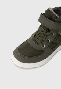 Sapatilha atlética verde com parte superior sintética, painéis texturizados, bico redondo, colarinho acolchoado, tira de velcro e sola de borracha branca.