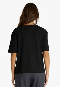 Maglietta nera a maniche corte realizzata in tessuto morbido, con scollo rotondo e vestibilità comoda, indossata con pantaloni grigi.