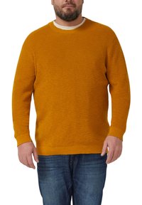 Dzianinowy sweter w kolorze musztardowej żółci z teksturowanym wzorem, okrągłym dekoltem oraz ściągaczami na mankietach i na dole; noszony na niebieskie dżinsy.