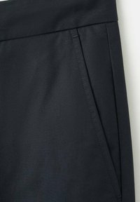 Close-up af mørkegråt tøjmateriel, der viser en skrå sidelomme med synlige syninger og detalje ved taljen.