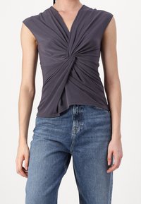 Haut sans manches gris foncé avec un détail noué à l'avant, associé à un jean bleu délavé taille haute, sur une personne debout.