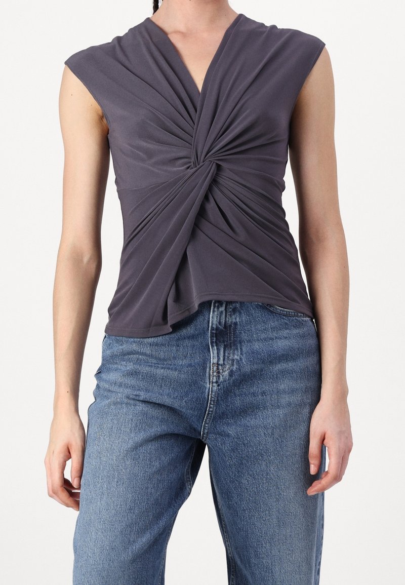 Haut sans manches gris foncé avec un détail noué à l'avant, associé à un jean bleu délavé taille haute, sur une personne debout.