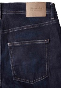 Tmavě modré džíny z denimu se zadní kapsou, se světle kontrastním prošitím a béžovou koženou nášivkou s embosovaným textem.