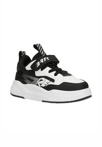 Baskets épaisses noir et blanc avec bride Velcro étiquetée « BRTK », lacets à l'avant et semelle épaisse blanche avec accents noirs et impression du logo.