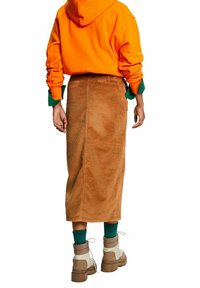 Oranger Hoodie, brauter Cordrock bis zur Mitte der Waden, klobige beigen Stiefel und grüne Socken. Hat eine weiche Textur und einen oversized Schnitt.
