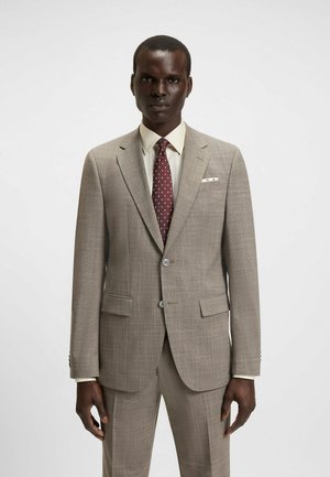 Light brown textured suit with notched lapels, two front pockets, and a white pocket square. Worn with a cream shirt and burgundy polka-dot tie.