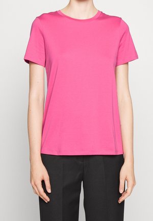 Camiseta de pecho redondo de manga corta en color rosa, hecha de algodón. Corte estándar con una textura suave y un diseño sencillo. Combinada con pantalones negros.