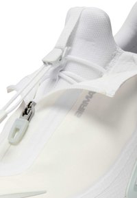 Lähikuva valkoisesta urheilukengästä, jossa on verkkomateriaalia päällisessä, valkoinen vetoketju ja nyörien säätöjärjestelmä, korostaen Air Max -brändäystä sivulla.