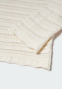 Beżowy sweter dzianiny z teksturowanym wzorem, z okrągłym dekoltem i ściągaczami przy mankietach, prezentujący otwartą strukturę tkaniny.