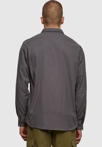 Szara koszula z długim rękawem o prostym kroju, zapinana na guziki przy mankietach, o miękkiej fakturze. Posiada klasyczny kołnierz i prosty design bez wzorów.