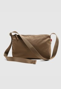 Καφέ τσάντα χιαστί από νάιλον με φερμουάρ, επίπεδο σχήμα και υφασμάτινο ιμάντα ώμου. Διαθέτει μικρό ετικέτα με το λογότυπο.