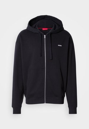 Svart zip-up hettegenser laget av myk stoff, med snøring i hetten, frontlommer og hvit "HUGO" logo på venstre bryst.