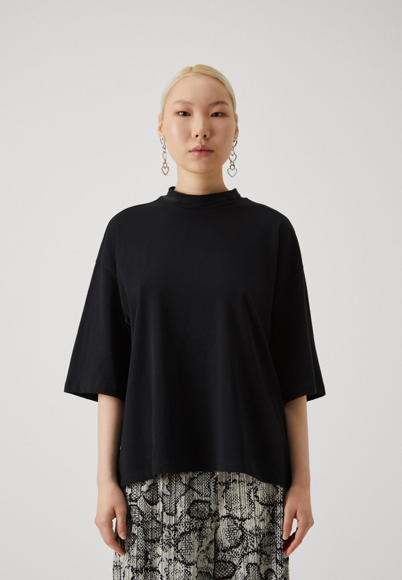 T-shirt noir oversize avec un col montant et des manches courtes, fabriqué en tissu doux. Associé à un bas clair à motifs.
