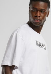 White cotton t-shirt featuring a black graphic print. Short sleeves and a relaxed fit with minimal stitching details.