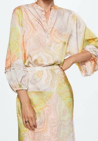 Vestido de manga larga con cuello camisero, que presenta un patrón de paisley en tonos pastel de rosa, amarillo y verde, hecho de una tela ligera.