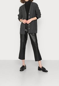 Kolgrå cardigan med V-ringning, knappframsida och ribbade ärmslut över en svart polotröja. Tillsammans med svarta läderbyxor i cropped modell och loafers.