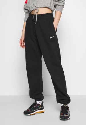 Sorte Nike joggingbukser med elastisk talje og lommer, med et hvidt logo på venstre side. Båret med sorte, multikolore sneakers.