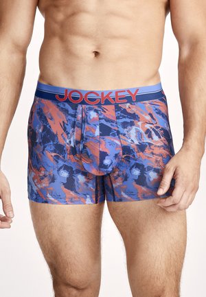Männlicher Oberkörper, der blaue und orange gemusterte Boxershorts mit einem blauen Bund trägt, auf dem „Jockey“ steht.