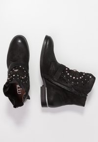 Black ankle boots with a textured finish, featuring decorative perforations and metallic accents. Short stacked heel and side zipper detail.