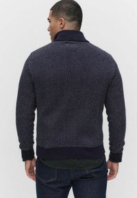 Mörkblå stickad tröja med ett strukturerat mönster och sjalkrage. Ribbad manschetter och nederkant, med små vita prickar som detalj.