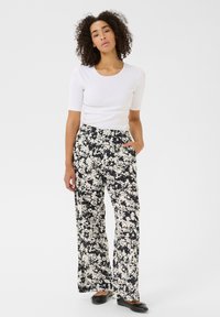 Pantalons larges à motif floral noir et crème en tissu léger, avec des poches latérales et une taille élastique. Associés à un haut blanc.