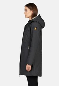 Zwarte waterdichte parka met capuchon, ritssluiting aan de voorkant, zijzakken en een logopatch op de mouw. Soepele textuur, knielang ontwerp.