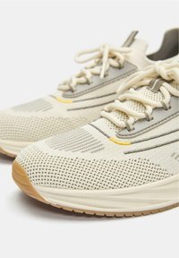 Lahke tekaške superge z zračno bež mrežasto zgornjico s sivimi poudarki, teksturirano srednjim podplatom in gumijastim podplatom gumijaste barve.