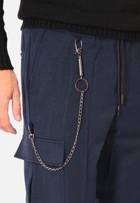 Pantaloni cargo blu navy con tasca con patta, catena d'argento attaccata e dettagli in metallo inclusi molla e portachiavi. Tessuto dalla texture liscia.