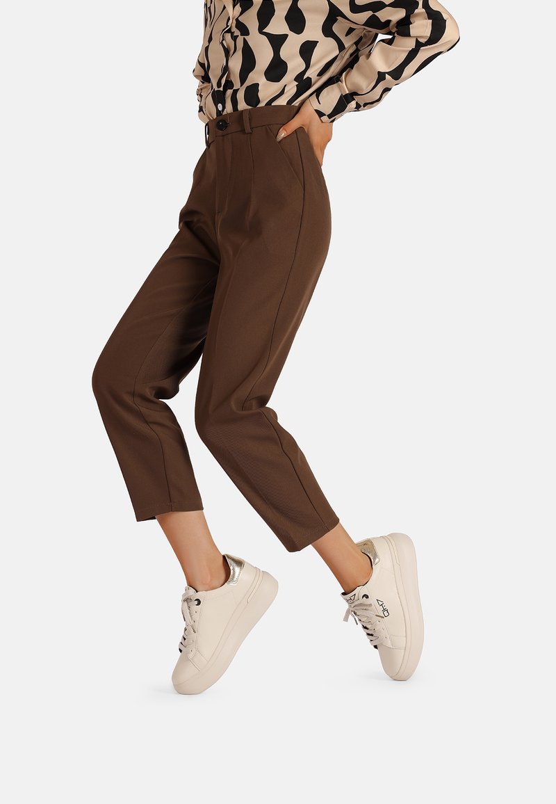 Pantaloni cropped marroni con cuciture frontali, abbinati a sneakers bianche con un accento metallico sul tallone. Modello in top fantasia.