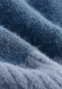 Zacht blauw wollen stof met een fuzzy textuur, met variërende tinten licht en donkerblauw, wat een gelaagde en uitnodigende uitstraling creëert.