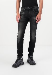 Black denim jeans with a slim fit, faded details, five-pocket design, and paired with black athletic shoes.
