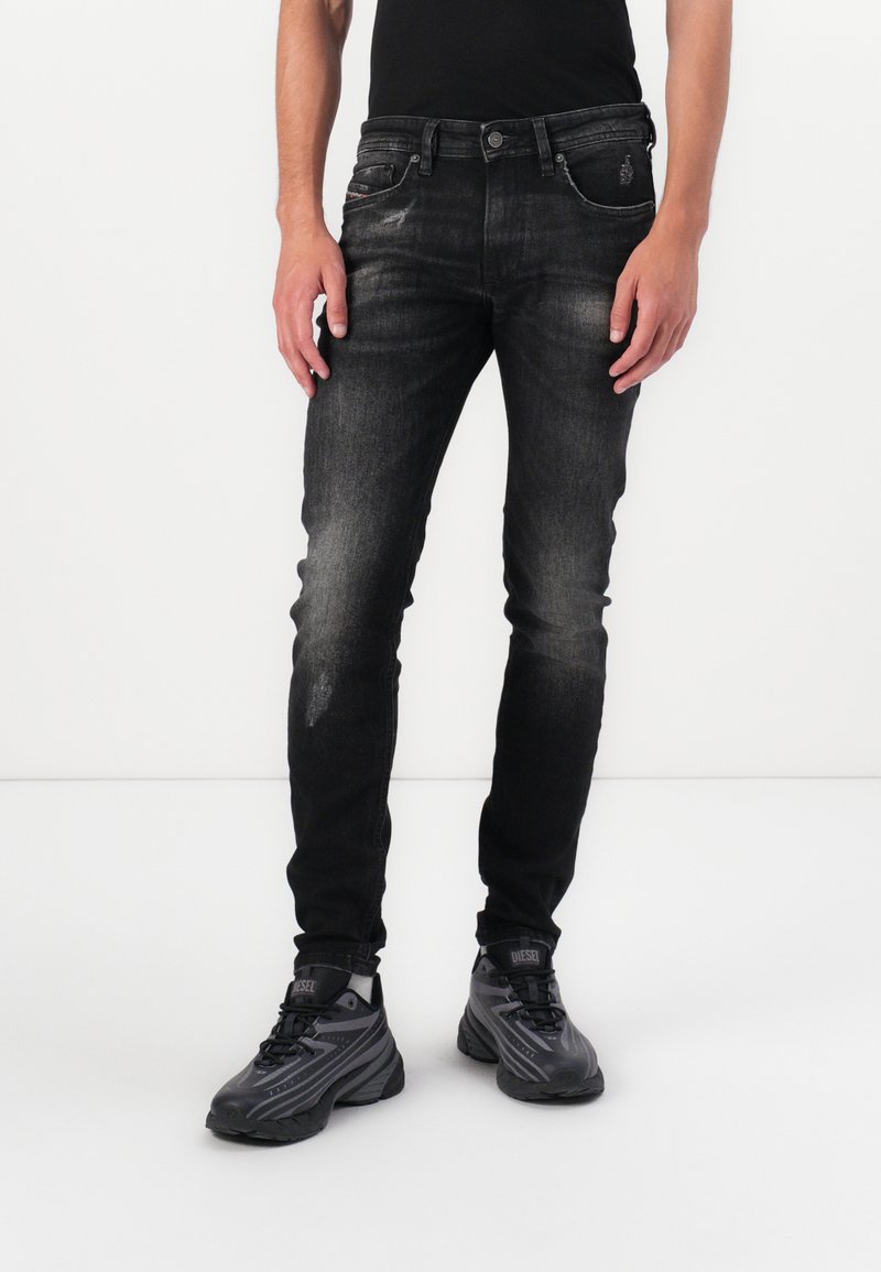 Jeanși negri din denim cu o croială slim, detalii decolorate, design cu cinci buzunare și asortați cu adidași negri.