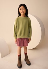 Grøn sweatshirt, lyserød fløjlsnederdel, brune leopardmønstrede støvler med sorte såler. Glat tekstur, afslappet pasform og legende designelementer.