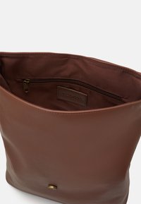 Sac en cuir marron avec une finition lisse et une fermeture éclair. L'intérieur présente une doublure en tissu et une petite poche zippée. Design simple.