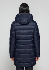 Marinblå puffjacka med huva, med en kviltad design och horisontell sömnad. Tyget ser glänsande och slätt ut.