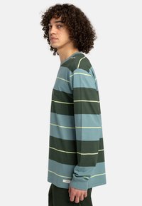 Langärmliges gestreiftes Hemd in Grüntönen und Blau, mit weißen horizontalen Streifen und einer kleinen Brusttasche. Weicher Baumwollstoff.