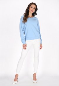 Felpa azzurro chiaro con maniche lunghe, scollatura rotonda e orlo a coste, abbinata a jeans bianchi aderenti e tacchi alti bianchi.