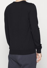 Pull noir en maille avec un col rond, des manches longues, et des poignets et un ourlet côtelés. Texture lisse et design minimaliste.