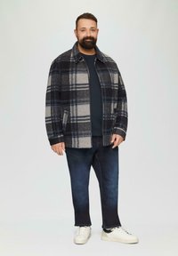 Karierte Jacke in Dunkelblau, Grau und Schwarz, aus Wollmischung, mit Kragen und Seitentaschen. Getragen über einem dunklen Oberteil und kombiniert mit dunklen Jeans und weißen Sneakers.